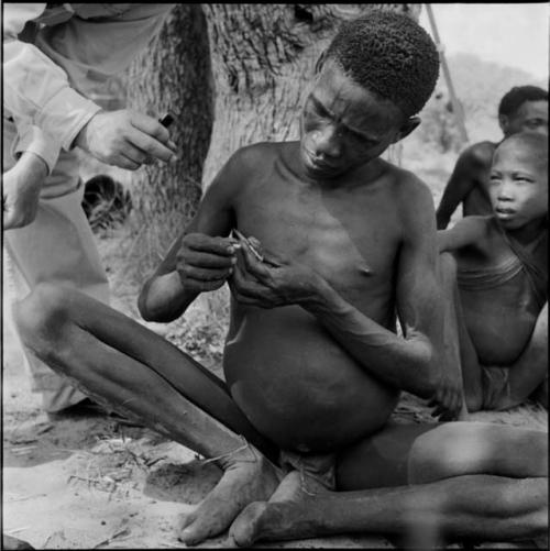 Man sitting, applying poison to an arrow point