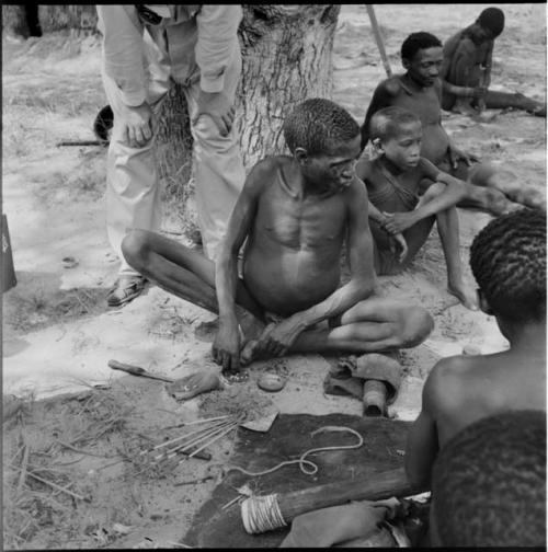 Man sitting, applying poison to an arrow point