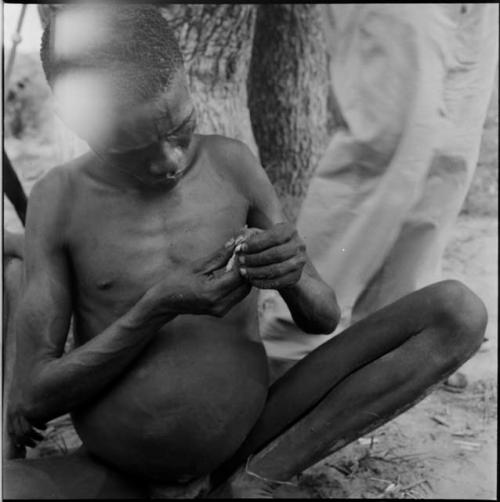 Man squeezing poison from a grub onto an arrow shaft