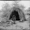 Man sitting next to a fire in front of his skerm, pounding with a mortar and pestle