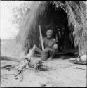 Man sitting next to a fire in front of his skerm, pounding with a mortar and pestle