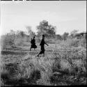 Two women, one carrying a baby in her kaross, walking in the veld