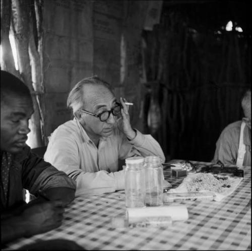 Kernel Ledimo and Charles Koch sitting at a table in the expedition tent with /Ti!kay and ≠Toma who are helping expedition members to identify insects