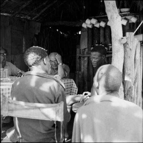 /Ti!kay and ≠Toma sitting at a table with expedition members, working with them to identify insects