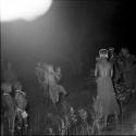 Children dancing in a line at a night dance, with a group of women dancing near them