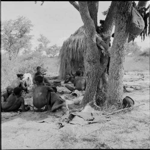 Group of men sitting and lying down next to a skerm, with strips of meat hanging from a tree near them