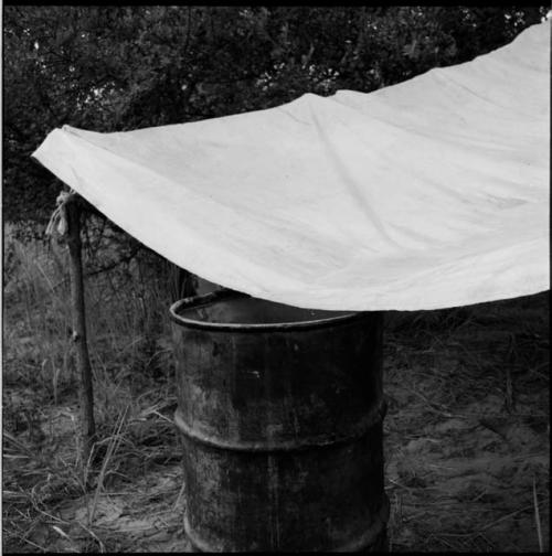 Expedition rain-saver constructed with canvas stretched across four posts, higher in the back, with a barrel at the lower end to catch the water