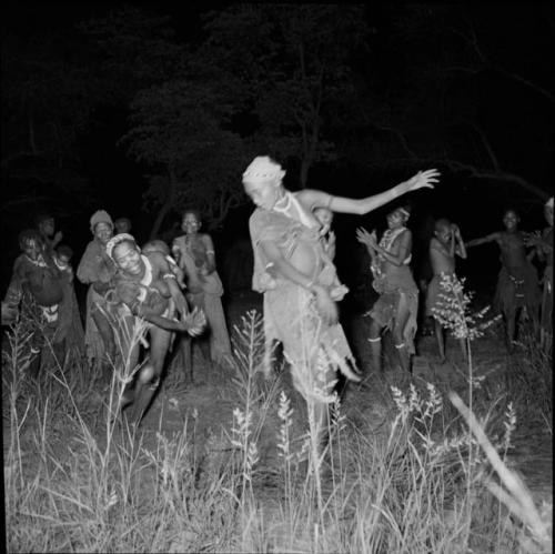 Two women dancing at a night dance, with a group of women clapping and singing, standing behind them