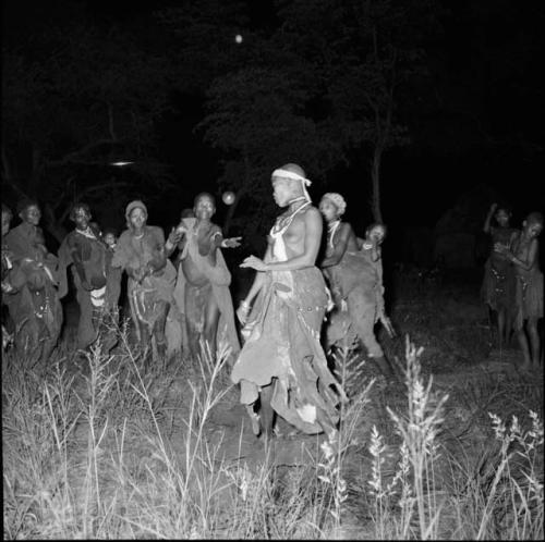 Group of women dancing, one tossing a ball, with a group of boys dancing in the background