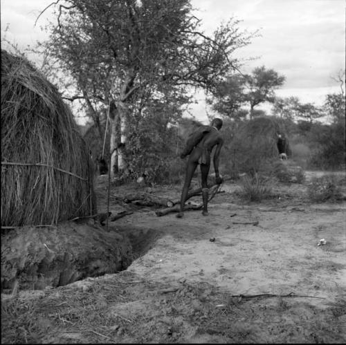 Man standing, pulling on a log on the ground near a skerm with a moat around it