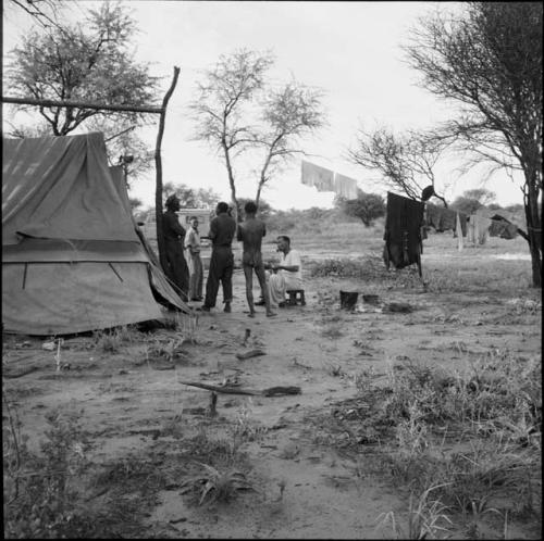 Group of men sitting and standing next to an expedition tent, with clothes drying on a line in the background