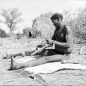 Man sitting on a hide he has been scraping, fixing his adze