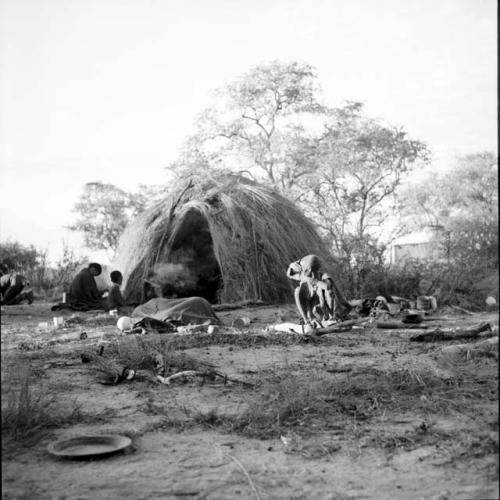 Family lying down and sitting near a skerm, with possessions on the ground around them