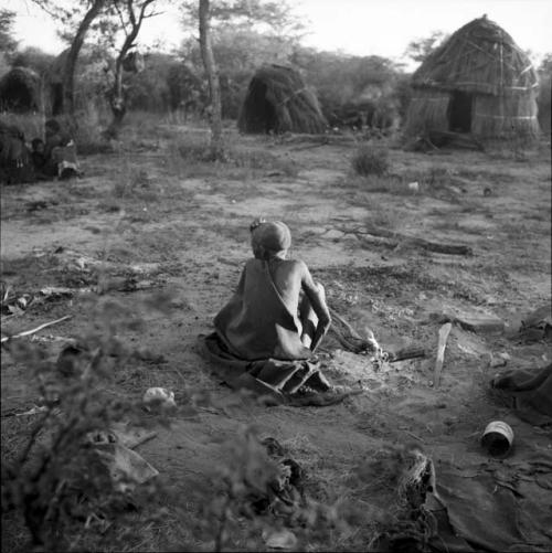 Woman sitting next to a fire, view from behind, with skerms in the background