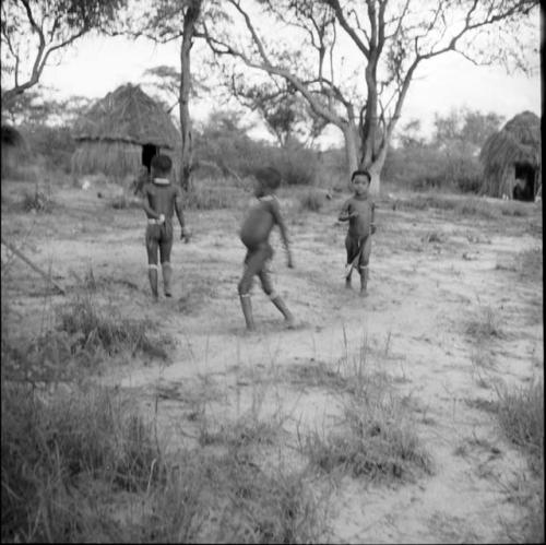 Three children playing tamah n!o’an (ball game) in the werft, with skerms in the background