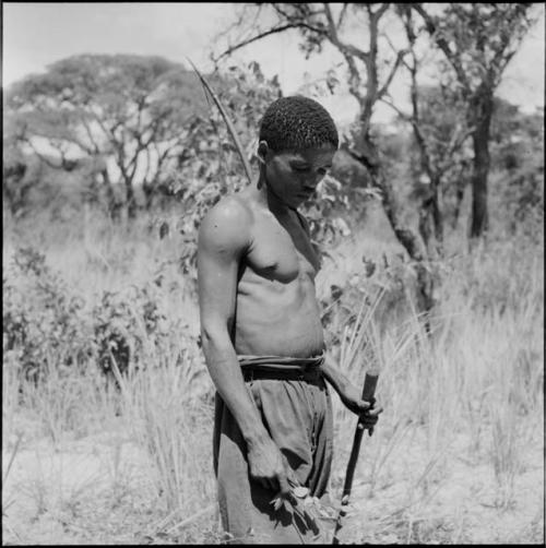 "Short /Qui" carrying his bow on his back, standing, looking at the ground