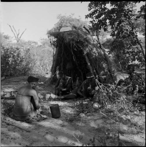 Two women and a child work with nuts near a shelter skerm with an enamel basin on top of it