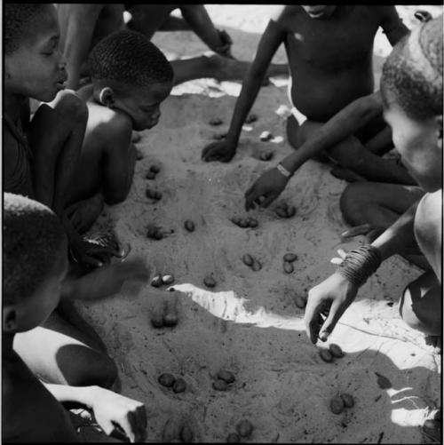 Group of boys playing /Ui (the counting game), with nuts in the holes in the sand, view from above
