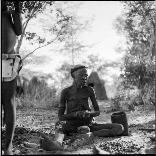 Woman sitting, cracking nuts, with her mortar on the ground next to her