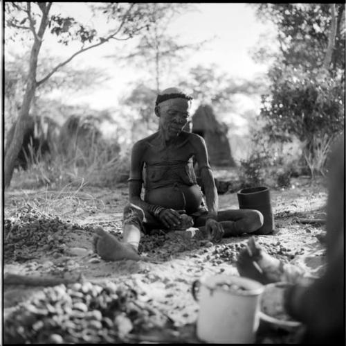 Woman sitting, cracking nuts, with her mortar on the ground next to her