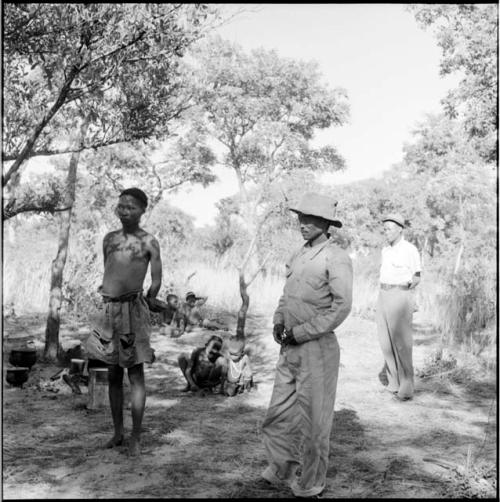 Bojo wearing Western clothing, standing with /Gunda, with a man and two groups of children in the background