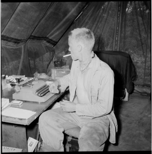 John Marshall sitting at a table with a typewriter on it, inside an expedition tent