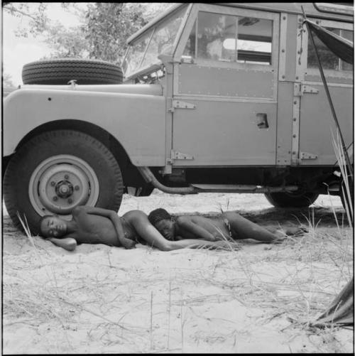 Two boys sleeping in the shade of the expedition Land Rover