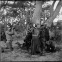 Group of women and girls playing Tcxai Djxani (a dancing game) at a tree, with John Marshall filming them