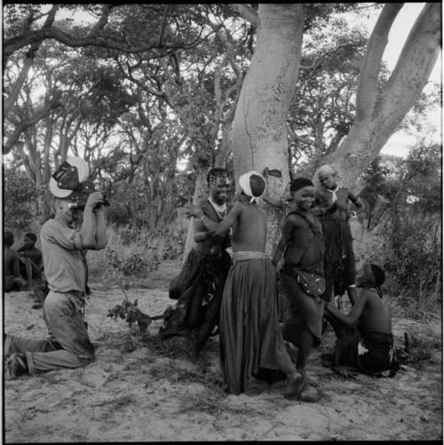 Group of women and girls playing Tcxai Djxani (a dancing game) at a tree, with John Marshall filming them