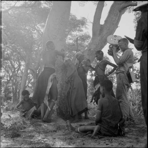 Group of women and girls playing Tcxai Djxani (a dancing game) at a tree, with John Marshall filming them