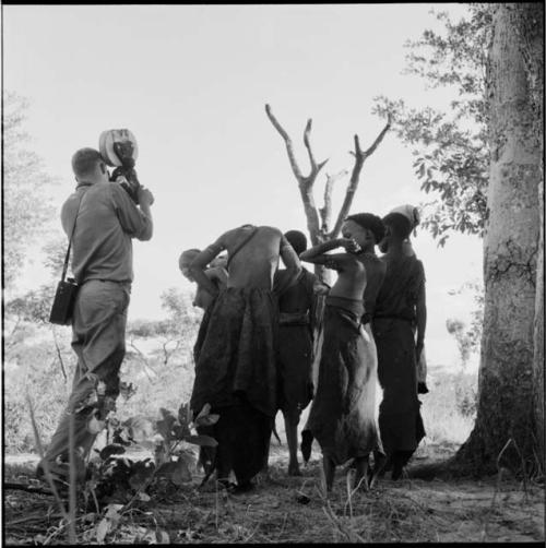 Group of women and girls playing Tcxai Djxani (a dancing game), with one holding another's arms behind her back, John Marshall filming them