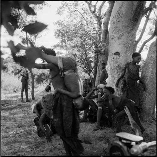 Group of women and girls playing Tcxai Djxani (a dancing game), with a girl carrying a child over her back, John Marshall filming them