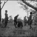 Group of women and girls playing khù n≠haru (skip-rope), with one girl leaning over N!ai, examining her foot