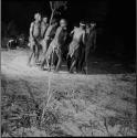 Group of men dancing in a line in a night dance, with the man in the center leaning forward