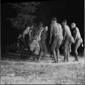 Men dancing in a circle in a night dance, facing a boy in the center of the circle