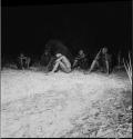 Six men sitting at the edge of the dance circle at a night dance