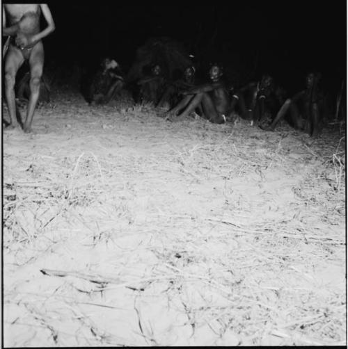 Dancer at a night dance standing, with a group of men sitting in the background