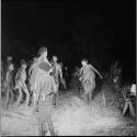 Two women dancing outside a circle of men dancing at a night dance