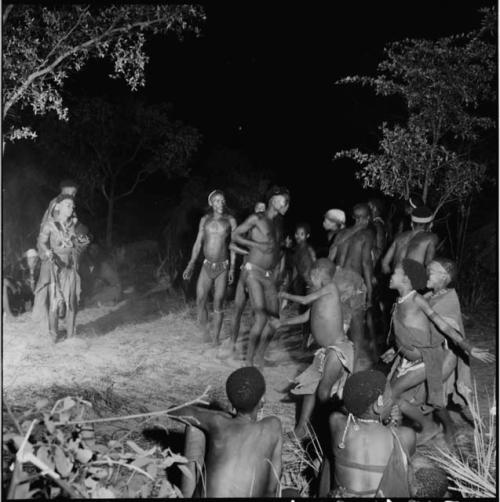 Woman carrying a baby dancing near a group of men and boys dancing in a night dance