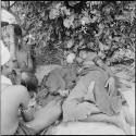 Woman lying down, a melon on the ground next to her head, next to a group of women sitting by a shelter skerm