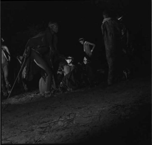 Men dancing in a night dance around a group of women sitting and clapping