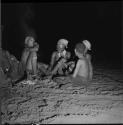 Three women and a boy sitting next to a fire at a night dance