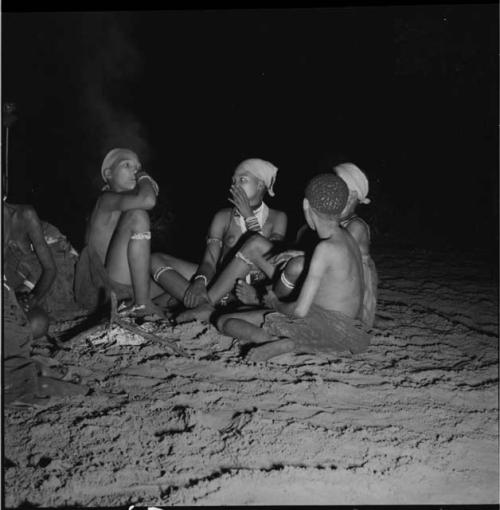 Three women and a boy sitting next to a fire at a night dance