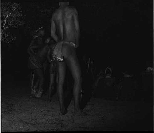 Group of men and boys standing next to three women and a boy sitting, at a night dance