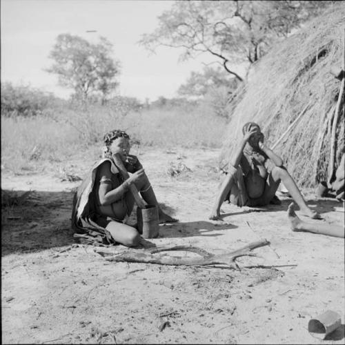 Woman eating food she has pounded with a mortar and pestle, sitting with another woman near a skerm