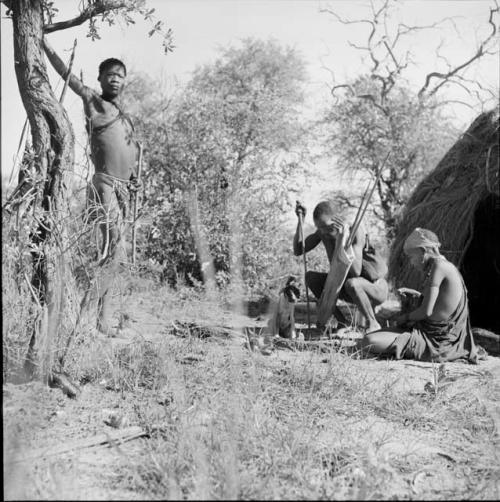 Man squatting next to his wife sitting in front of a skerm, with a man standing near them, dog sitting next to them