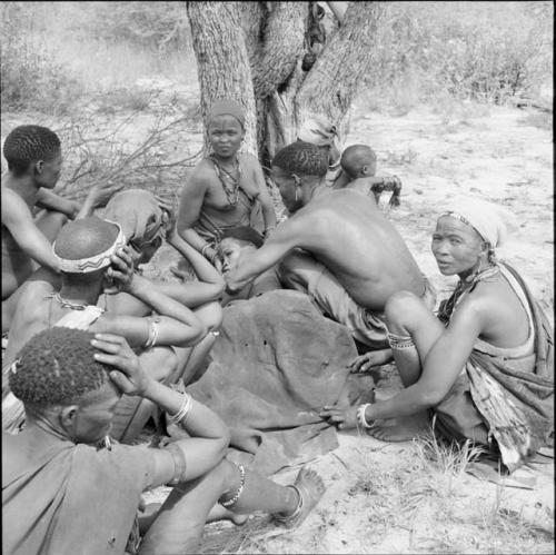 /Ti!kay curing a woman who is lying sick in a circle of women sitting, close-up