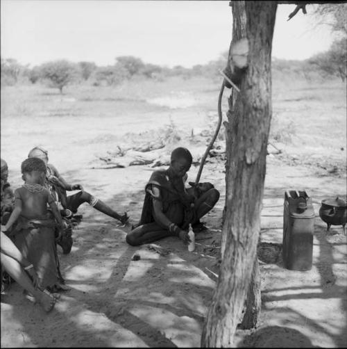 Women and children sitting in the expedition camp, one holding a Western baby bottle full of milk