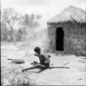 Man sitting in front of a skerm, cracking mangetti nuts with a rock