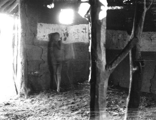 Boy standing next to drawings he and other children made on a wall inside a hut